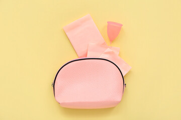 Lady's cosmetic bag with menstrual cup and pads on pale yellow background