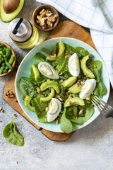 Healthy food, summer healthy eating. Organic green avocado and spinach salad with eggs, green beans, nuts on a stone table. View from above. Copy space.