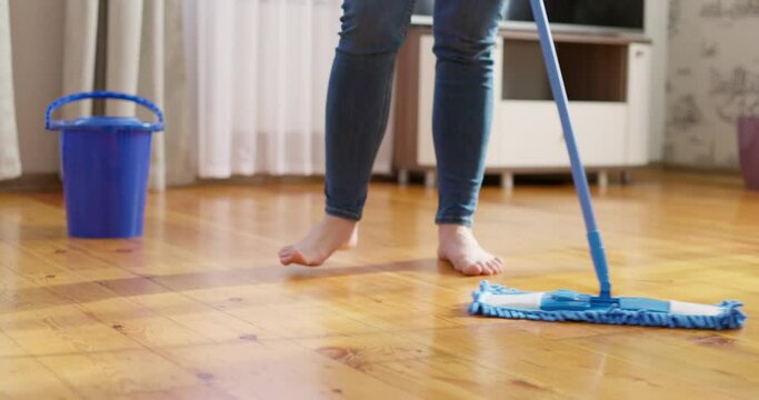 Woman in casual clothes washing a wooden floor with a damp microfiber mop