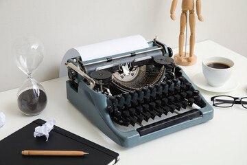 Vintage typewriter with cup of coffee, wooden mannequin and notebook on white table near wall