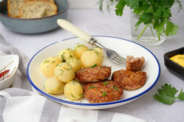 Plate with cutlets, boiled baby potatoes and dill on white grunge table in kitchen