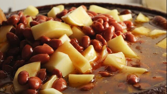 In cholent, chicken and potatoes in spices with beans are mixed with a wooden spatula. close-up