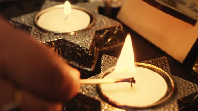 A woman's hand lights candles on the eve of Shabbat in candlesticks in the shape of a star of David. Medium plan