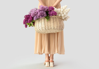 Young woman with basket of lilac flowers on light background, back view