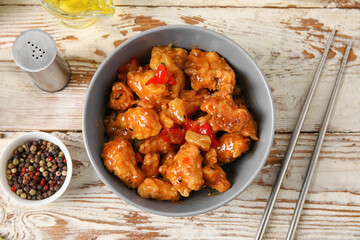 Tasty sweet and sour chicken in bowl with spices on light wooden background, closeup