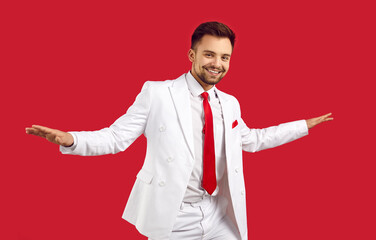 Cool cheerful guy in white formal suit dances and rejoices isolated on red background. Attractive...
