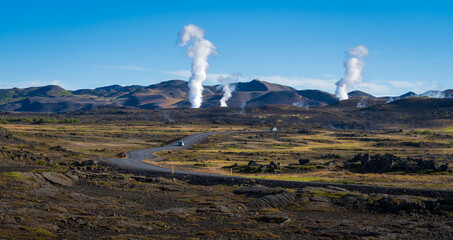 Asphalt road in Iceland in Mývatn geothermal area.  steam from geothermal power station.