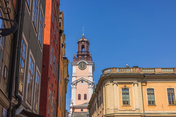 View up to roofs of old buildings. Big wall clock on tower of building on blue sky background. Sweden. Stockholm.