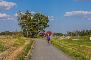 View of woman on bicycle on bicycle paved road on summer day. Sweden. 