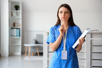 Thoughtful female medical intern with clipboard at hospital