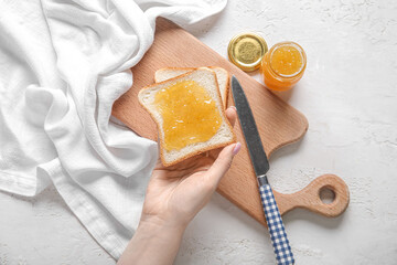 Woman holding tasty toast with peach jam on grunge white background