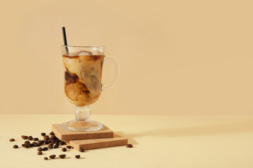 Glass of ice coffee with straw and beans on yellow table near beige wall