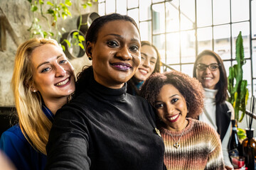 Multiethnic female friends taking selfie while smiling on camera in the modish office - Happy...