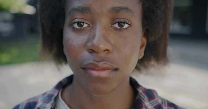 Close-up portrait of sad African American person looking at camera with upset expression in city. Negative emotion and beautiful woman concept.