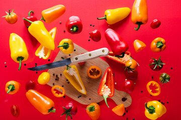 Fototapeta na wymiar sweet peppers and red tomatoes on a cutting board. Knife and slices of fresh vegetables. levitation on a red background. View from above