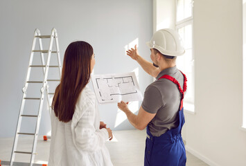 Foreman showing to a young homeowner woman blueprint with design project or repair of her new...