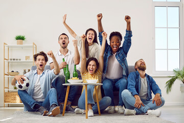 Happy excited people watching football on TV. Ecstatic euphoric overjoyed diverse male and female friends sitting on sofa at home, watching soccer, celebrating victory, raising hands up and screaming
