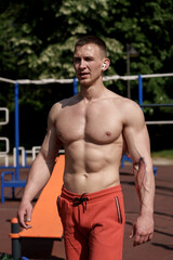 Muscular male athlete with naked torso standing on sports ground and looking away on sunny summer day