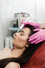 Fototapeta premium Ultrasonic facial and chin peeling for girl with ultrasonic scrubber in cosmetology clinic. Cleansing facial skin and removing blackheads with ultrasonic scrubber.