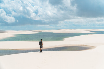 Man in the sand dunes next to a lagoon with white sand at Lencois maranhenses national park in Brazil.