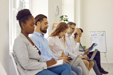 Multiracial business people making notes on corporative education sitting in row in office. They make notes in notebooks, laptop, record on a dictaphone. Training, seminar, workshop, master class.