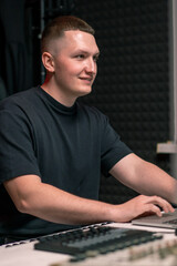 young smiling sound engineer in recording studio mixing tracks working with laptop recording song