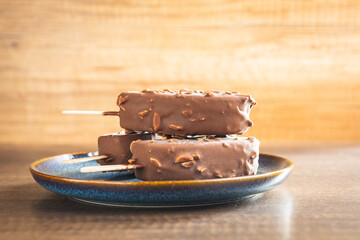 Popsicle, ice cream covered with chocolate on wooden table.