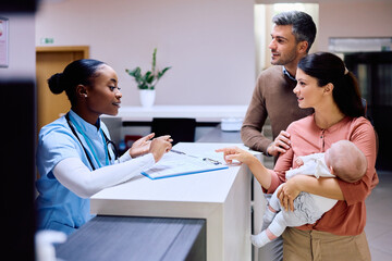 Parents with baby talk to reception nurse at family doctor's office.