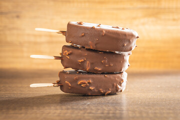 Popsicle, ice cream covered with chocolate on wooden table.