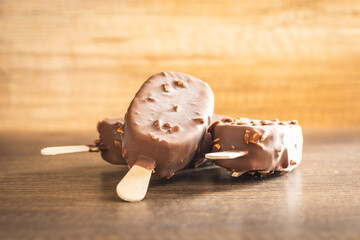 Popsicle, ice cream covered with chocolate on wooden table.