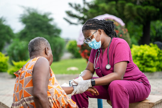 image of african young nurse in facemask, diagnosing senior woman outside- homecare service concept