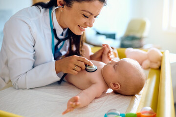Happy pediatrician using stethoscope during baby's regular health checkup ay doctor's office.