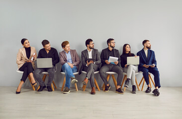 People waiting for a job interview. Group of young men and women with CVs and laptops sitting in...