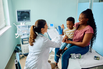 Happy black boy gives high five to his pediatrician after medical examination at doctor's office.