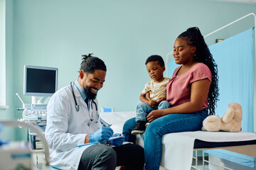 Black mother and son talk to pediatrician at medical clinic.