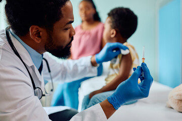 Black pediatrician giving vaccine to child at doctor's office.