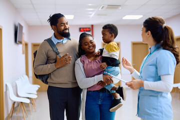 Happy black family talks to nurse in hallway at doctor's office.