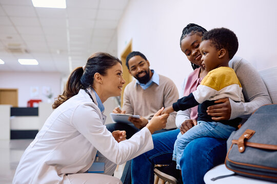 Female pediatrician talks to black little boy who is sitting on mother's lap at clinic.