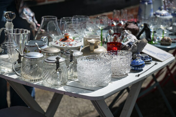 Glass dishes, beer mugs and drinking glasses as well as other tableware on a table at a flea market on a sunny day, selected focus