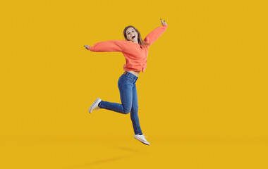 Fototapeta na wymiar Cheerful funny young woman jumps and stretches her arms isolated on bright yellow background. Happy woman in casual clothes jumps celebrating her success and victory. Concept of human emotions.