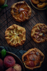 Different homemade baked fruit tarts, galettes with apricot, peach and apple on dark background