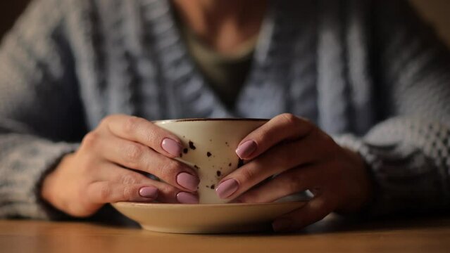 Close-up of a woman hands holding mug of hot drink that standing on wooden table