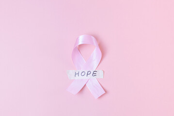 Pink ribbon with sticky tape and the word: hope on a pink background.