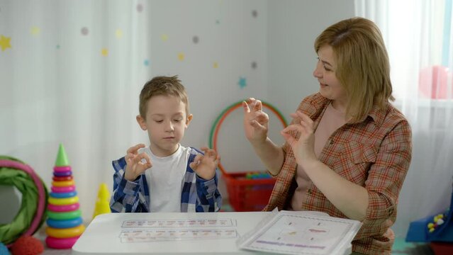 A Caucasian boy works with a speech therapist in the classroom. The child learns to pronounce letters and sounds correctly with a professional. High quality 4k footage