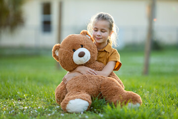 Happy child girl hugging her teddy bear friend outdoors on green grass lawn. Friendship concept