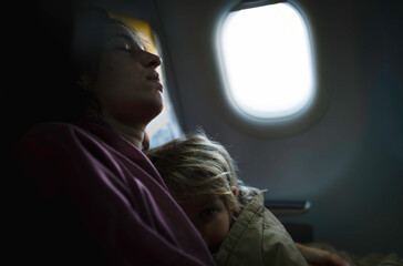 mother sleeps with her three year old daughter during an airplane ride. kid in mother's arms on plane.