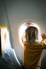 A three years old baby boy curiously looking through airplain's window.