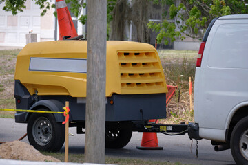 Utility van with yellow compressor trailer with jackhammer machine on road construction site