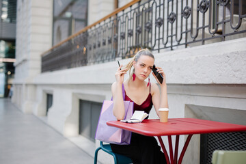 Young woman sitting at table writing notes using her cell phone