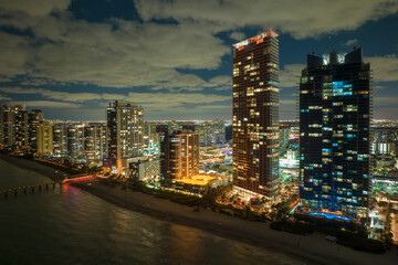 View from above of brightly illuminated high skyscraper buildings in downtown district of Sunny Isles Beach city in Florida, USA. American tourist urban district at night